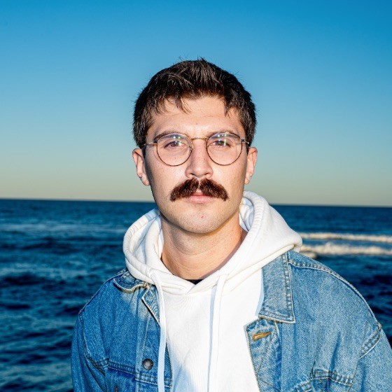 Photo of Ben in front of the ocean, looking at the camera.