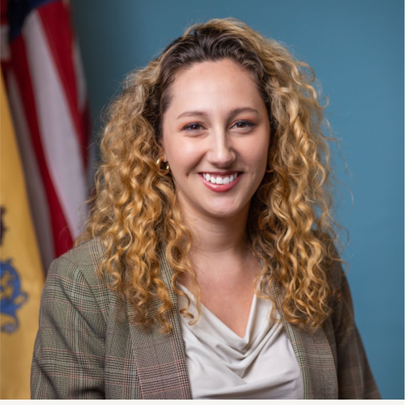 Portrait of Sunni Vargas in front of the NJ and US flags.